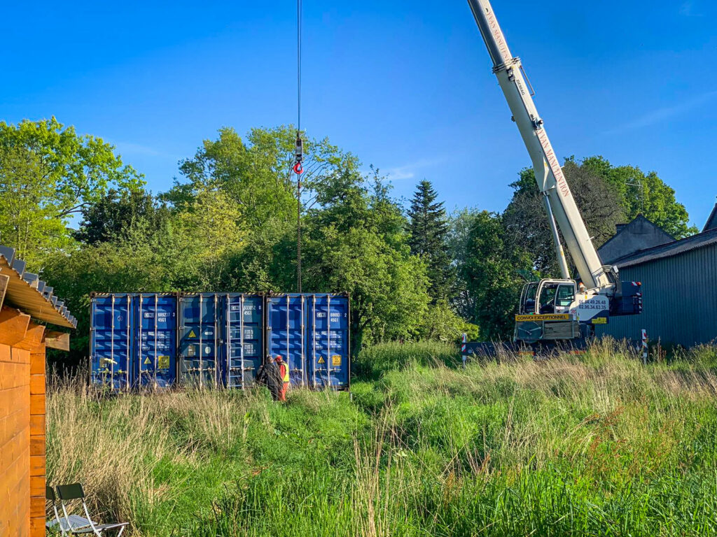 Grue soulevant un container maritime de 40 pieds HIGH CUBE pour un projet de transformation en maison durable par un client à Saint-Malo-Les-Trois-Fontaines.