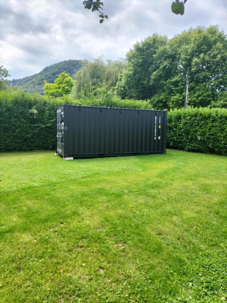 Container de 20 pieds noir utilisé comme abri de jardin, installé dans un jardin verdoyant à Marnoz.