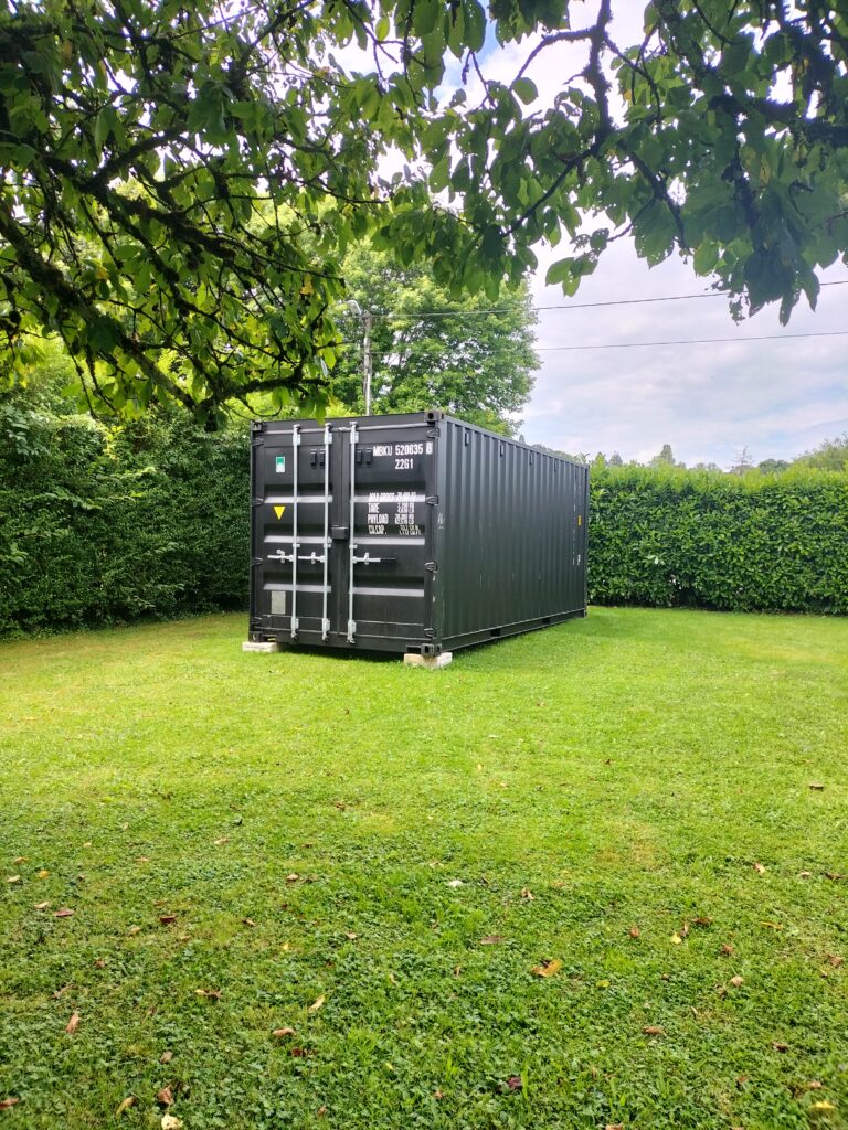 Container de 20 pieds noir utilisé comme abri de jardin, installé dans un jardin à Marnoz.