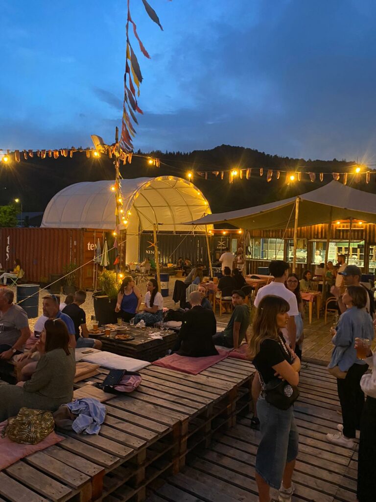 Ambiance festive au bar guinguette en container du Trente-Trois à Pratz, avec terrasse en bois, guirlandes lumineuses et invités en soirée.