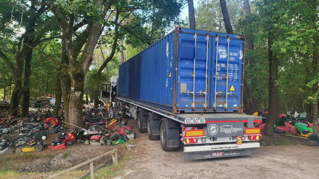 Camion transportant un container 40 pieds d'occasion bleu à travers un chemin étroit bordé d'arbres chez NICO BRICO 24.