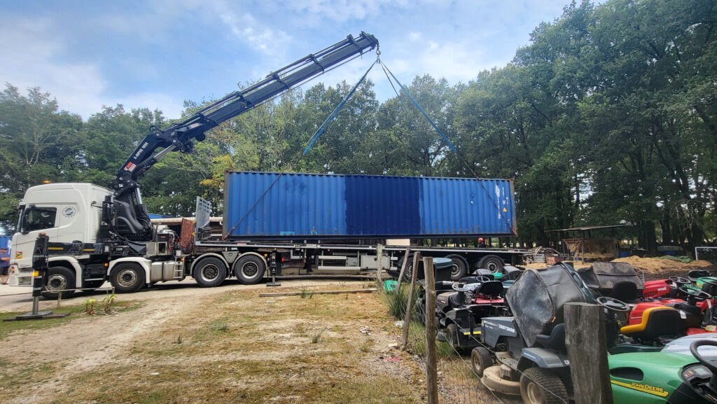 Grue soulevant un container 40 pieds d'occasion bleu pour le déposer chez NICO BRICO 24.