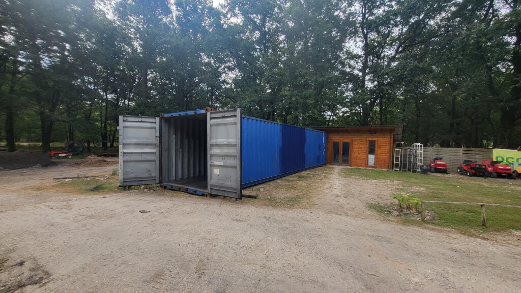 Container 40 pieds d'occasion bleu ouvert, livré par In'Box Container chez NICO BRICO 24, à côté d'un bâtiment en bois.