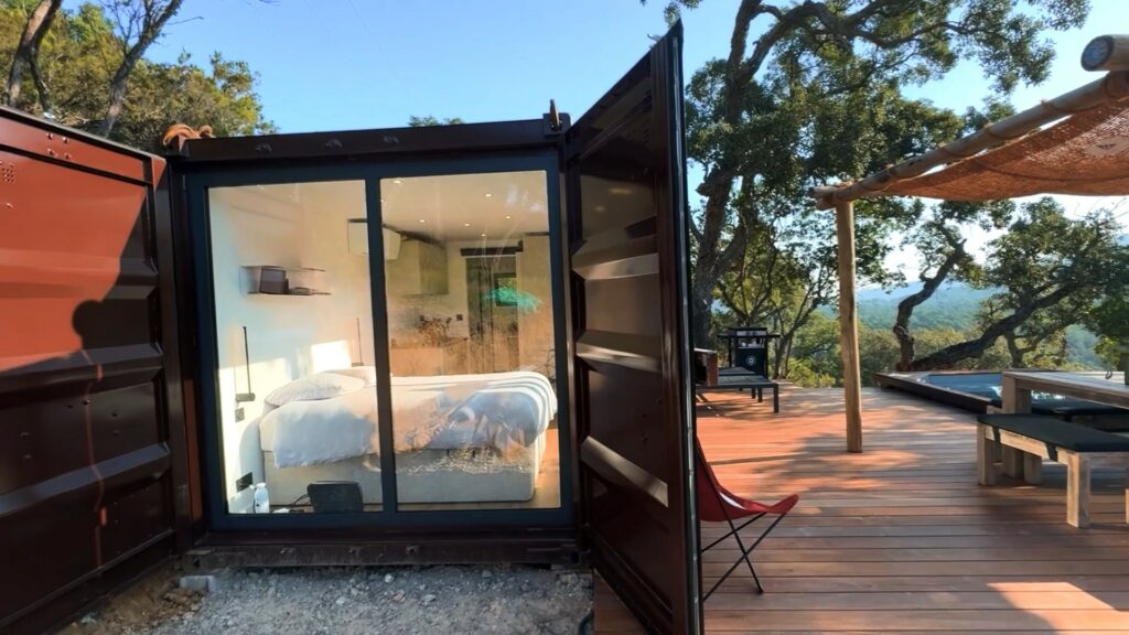 Gîte en container 20 pieds avec une baie vitrée donnant sur une terrasse en bois, dans un cadre naturel à La Môle.