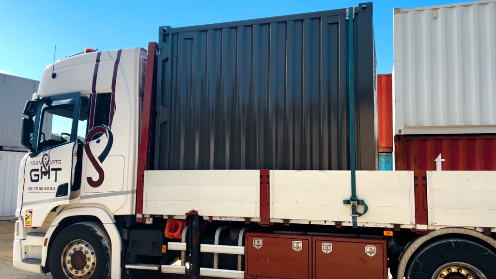 Un container 10 pieds gris chargé sur un camion de la société GHT, prêt pour la livraison dans un environnement industriel.