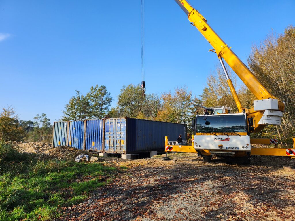 Une grue jaune stationnée devant une pile de containers 40 pieds HC en cours d’installation sur un chantier à Cornille, Dordogne.