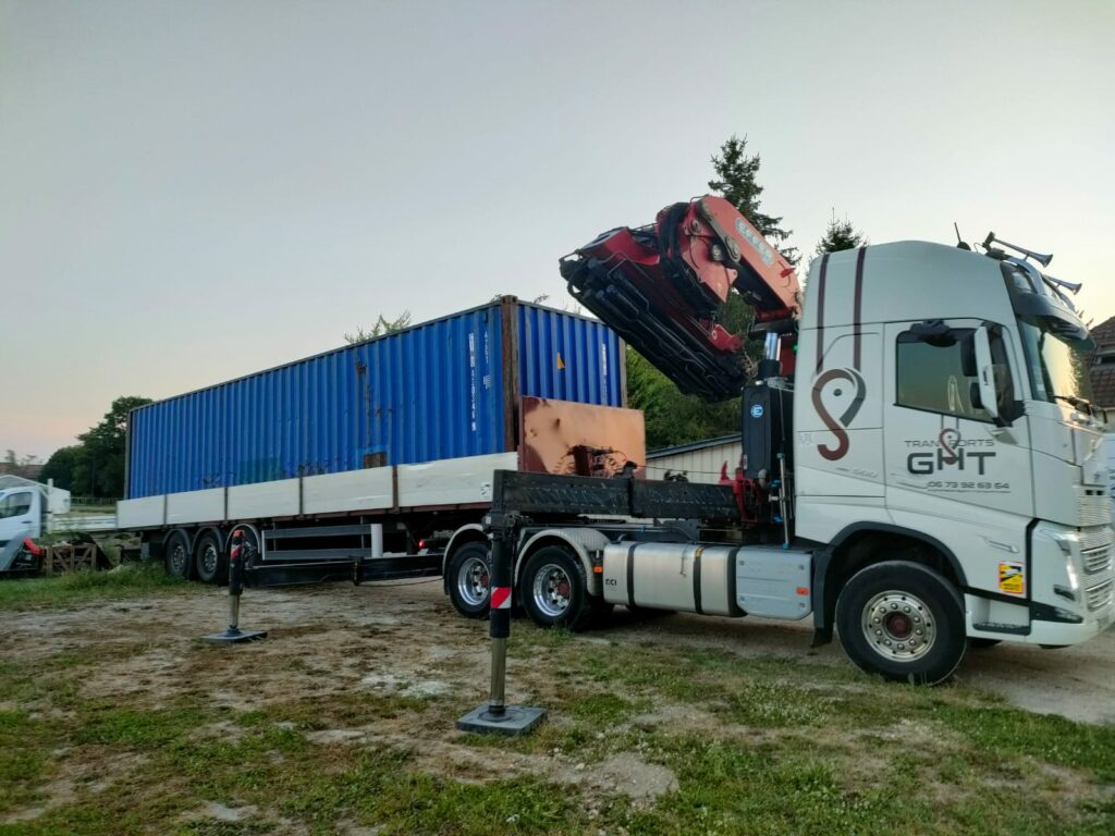 Un container maritime bleu de 40 pieds installé sur une remorque, prêt pour le transport ou le stockage, avec un camion équipé d’une grue de la société GHT.