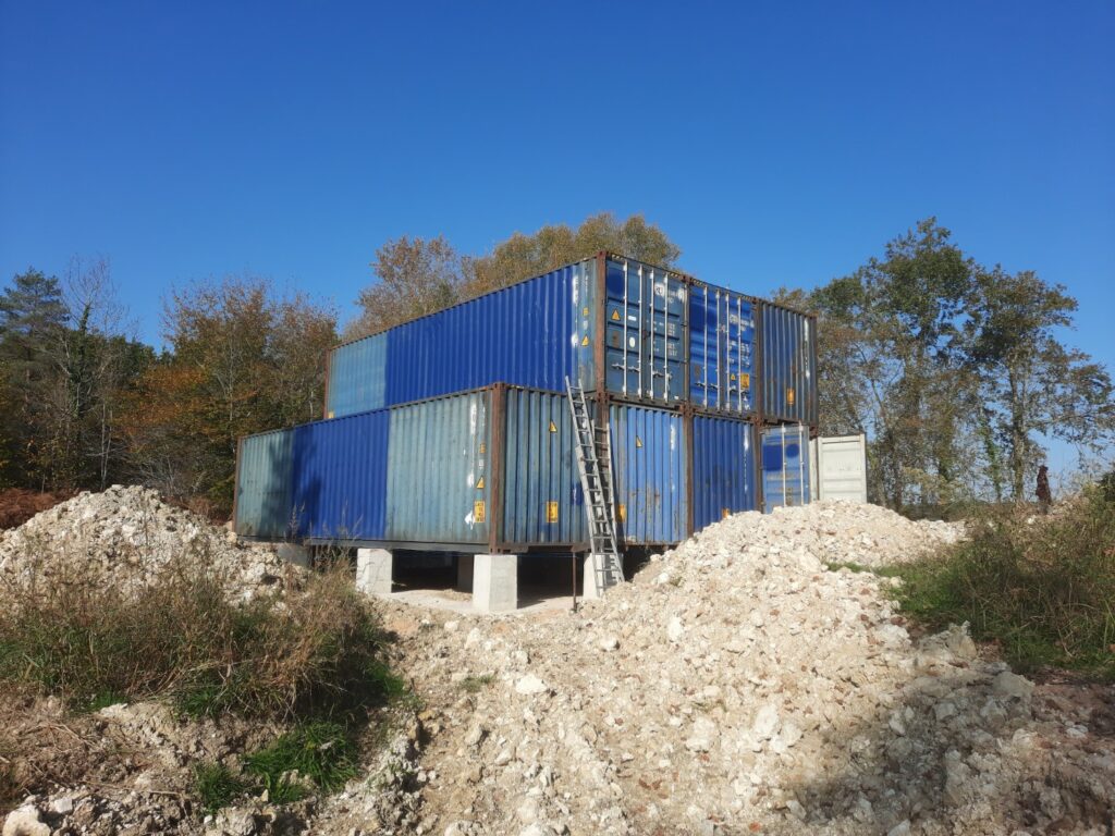 Sept containers 40 pieds HC empilés sur des blocs de béton, installés sur un terrain en cours de préparation à Cornille, Dordogne.